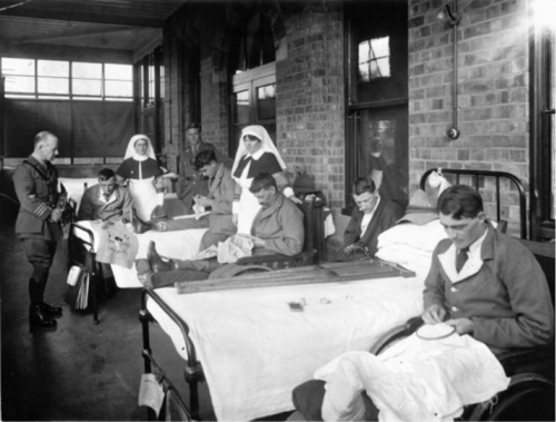 A black and white photo of  returned servicemen embroidering in hospital beds, surrounded by nurses