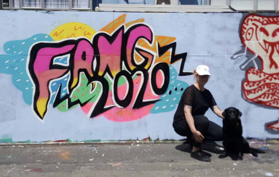 Pinky and her black guide dog pose in front of one of her artworks that reads "Fang 2020"