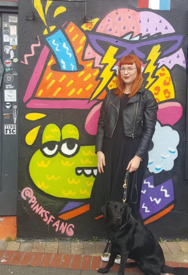 Pinky and her guide dog Lyric stand in front of another of her artworks