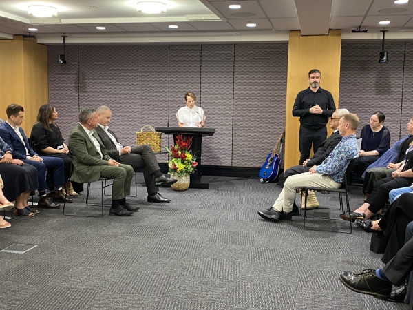 Paula Tesoriero standing behind a lectern speaking at the Mihi Whakatau event. People are sitting on two sides of the room in front of her (MSD staff and Whaikaha staff) and an NZSL interpreter is on the right.